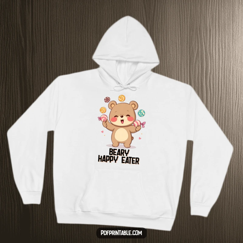 Funny hoodie featuring a delighted bear character expertly juggling a cascade of large, colorful candies, exuding joy and a playful, sweet-loving attitude.